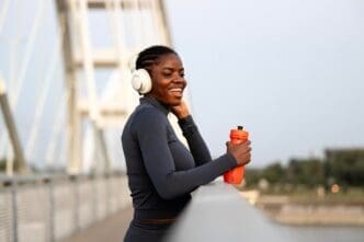 A smiling Black woman in athletic wear uses a smartphone while taking a break from training.