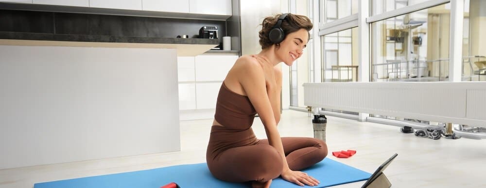 Smiling brunette woman wearing headphones watches a video on a tablet.