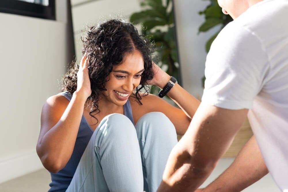 A woman smiles as she does situps with a partner holding her feet during a home workout.