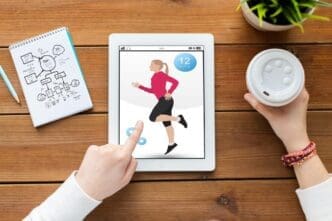 A woman uses a tablet displaying a fitness app, with a notebook and coffee on a wooden table.