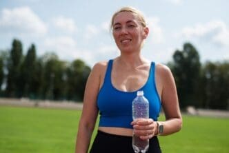 A woman in athletic wear takes a drink from a water bottle at a stadium, appearing tired after a workout.