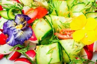 A colorful spring salad with fresh vegetables and edible flowers is arranged on a table.