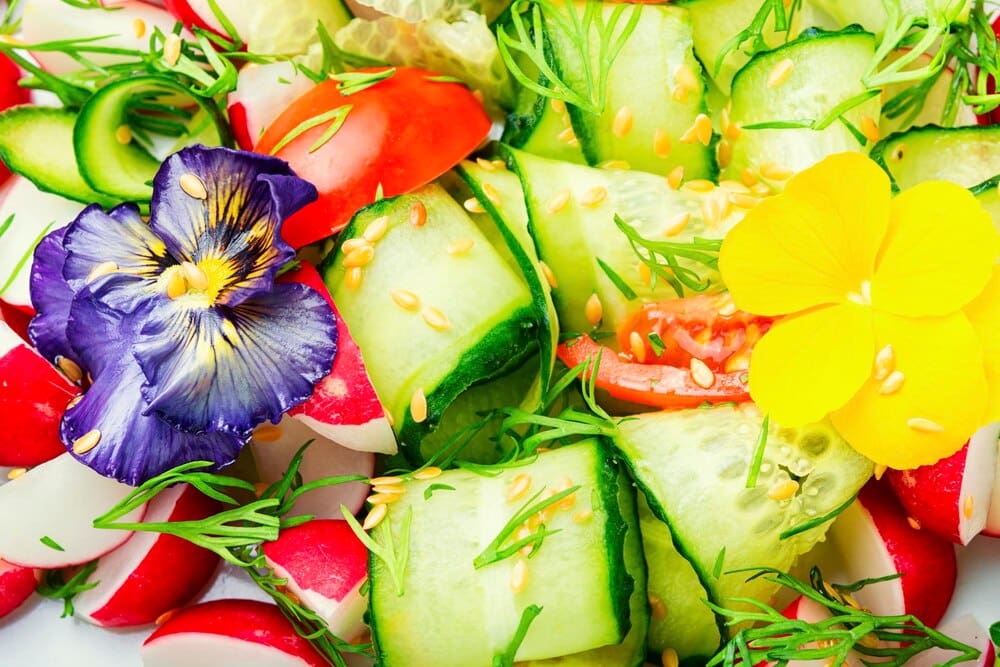 A colorful spring salad with fresh vegetables and edible flowers is arranged on a table.