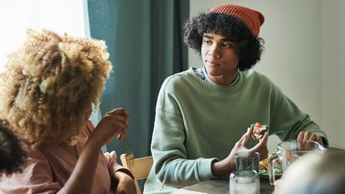 A teenage boy and his mother sit at a table, engaged in conversation during a home dinner.