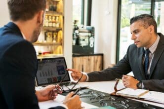 Two businessmen sit at a cafe table, engaged in a meeting with a laptop.