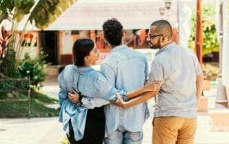 A woman walks in a park with her boyfriend while holding hands with another man, illustrating a love triangle.
