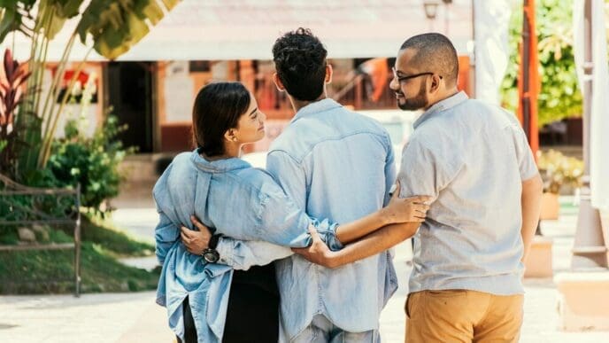 A woman walks in a park with her boyfriend while holding hands with another man, illustrating a love triangle.