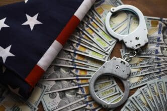 A pair of handcuffs rests on a U.S. flag, with money scattered around, illustrating concepts of law enforcement and financial crime.