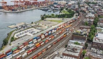 A wide view of the Vancouver Port shows a container port terminal and freight station with trains and tank cars.