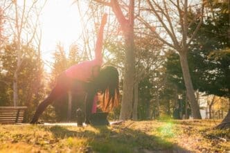 A woman performs yoga exercises in a park as the sun sets.