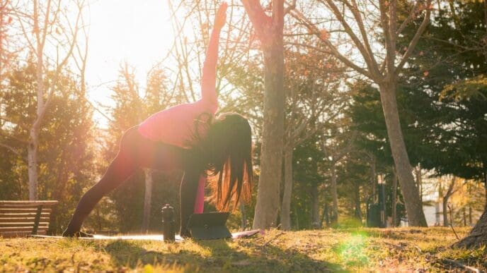 A woman performs yoga exercises in a park as the sun sets.