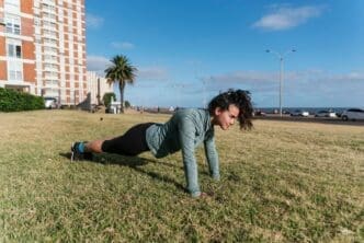 A woman in workout clothes performs push-ups on a grassy surface.