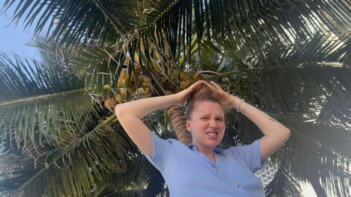 A woman hides her head under a coconut tree, shielding herself from falling coconuts.