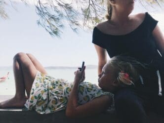 Woman sitting by the sea, holding a mobile phone, with the sky in the background.