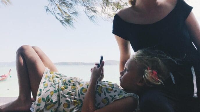 Woman sitting by the sea, holding a mobile phone, with the sky in the background.