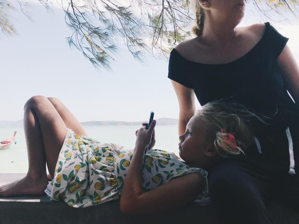 Woman sitting by the sea, holding a mobile phone, with the sky in the background.