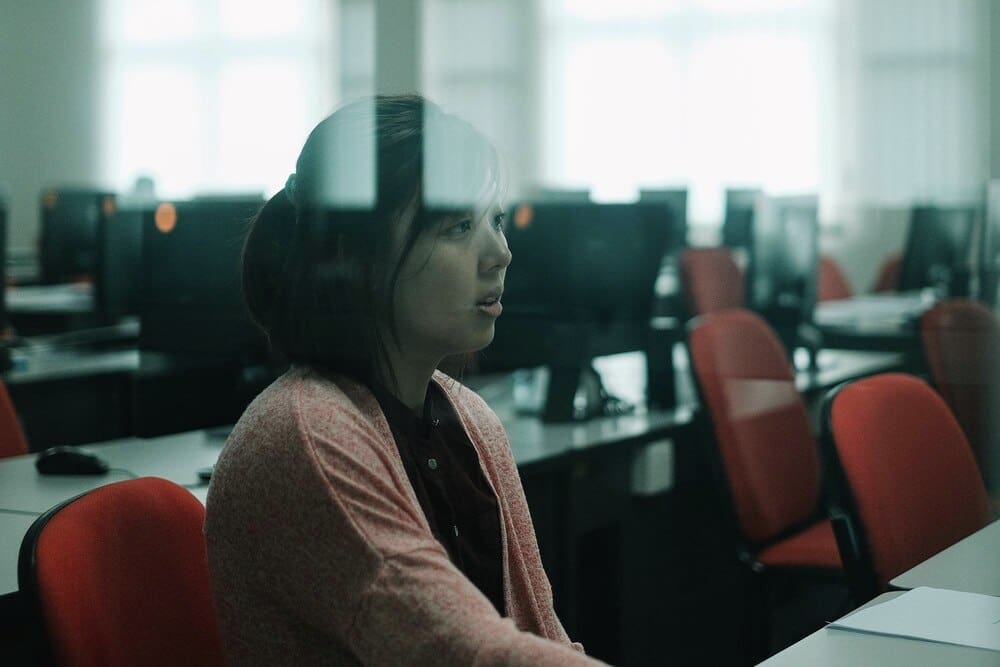 A woman sits at a desk in a classroom.