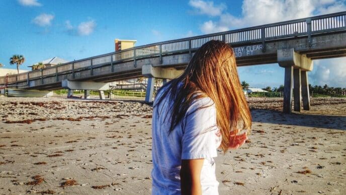 Woman stands on the sand in front of a pier on a sunny beach.