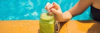 Woman holding a green spinach and banana smoothie with a pool in the background.