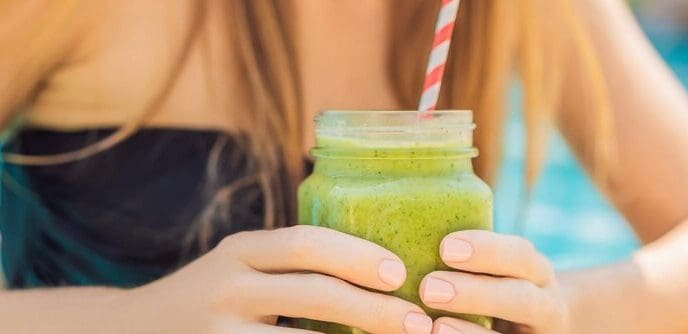 A woman holds a green smoothie made with spinach and banana near a swimming pool, representing healthy eating.