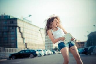 A young woman with long, curly hair and a hipster style listens to music.