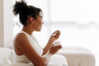 A young Black woman smiles while eating yogurt in her sunny kitchen.