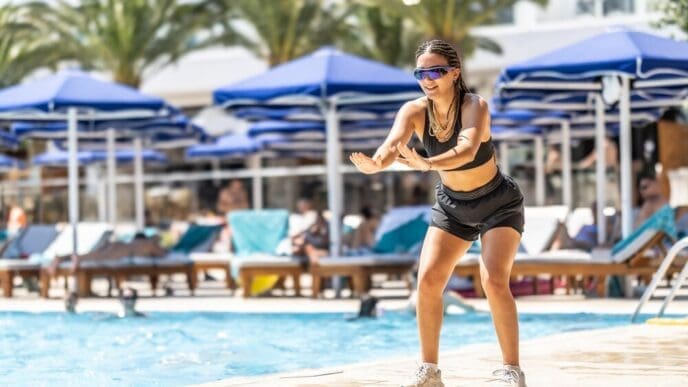 A young woman animates water aerobics for people in a hotel resort pool.