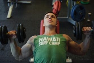 A young man lifts dumbbells while working out at a gym.