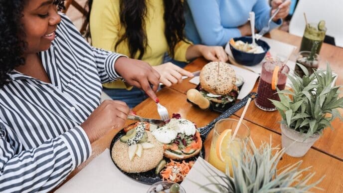 A young Black girl's right hand rests on a table, likely as she enjoys breakfast with friends on an outdoor restaurant terrace.