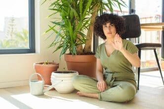 A young Arab woman waters plants with a watering can inside a home.