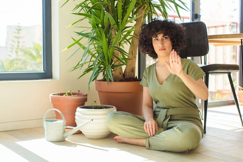 A young Arab woman waters plants with a watering can inside a home.