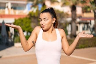 A young, pretty brunette woman raises her hands with a doubtful expression.