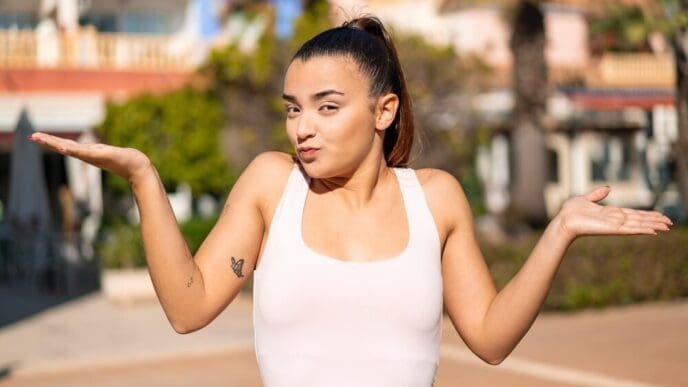 A young, pretty brunette woman raises her hands with a doubtful expression.