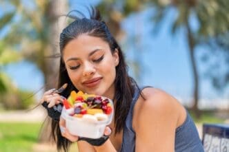A young woman smiles while holding a bowl of fruit outside.