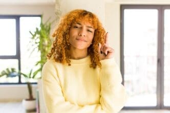 A young, attractive Latina woman with red hair smiles in a modern home.