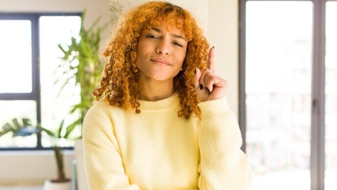A young, attractive Latina woman with red hair smiles in a modern home.