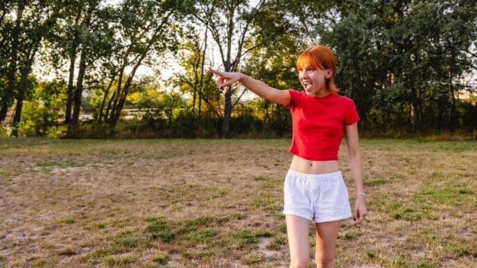 A young woman with her arm raised, pointing and shouting in a park at sunset.