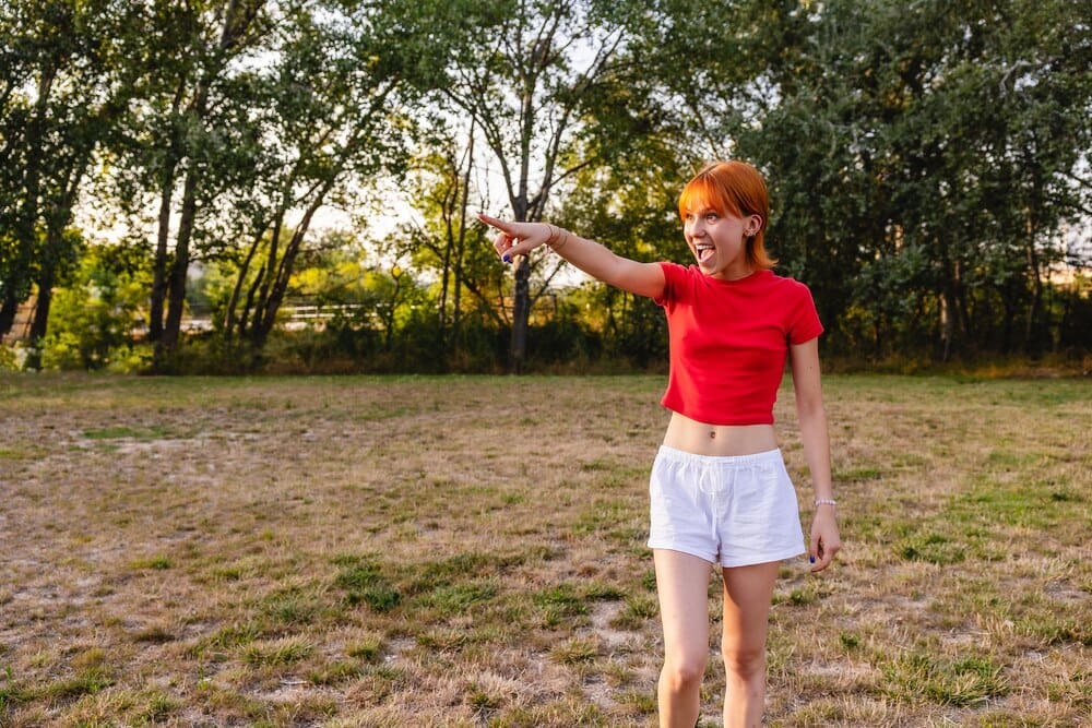 A young woman with her arm raised, pointing and shouting in a park at sunset.