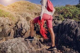 A young woman climbs a rope up a mountain, with the ocean visible in the background.