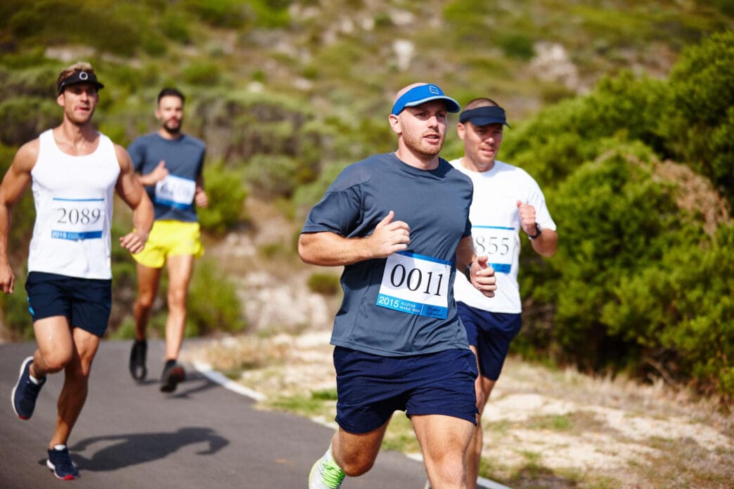 Runners with bibs participate in a 100-mile race on a paved road with greenery