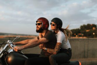 A bearded man and a woman ride a motorcycle together in the late afternoon sun
