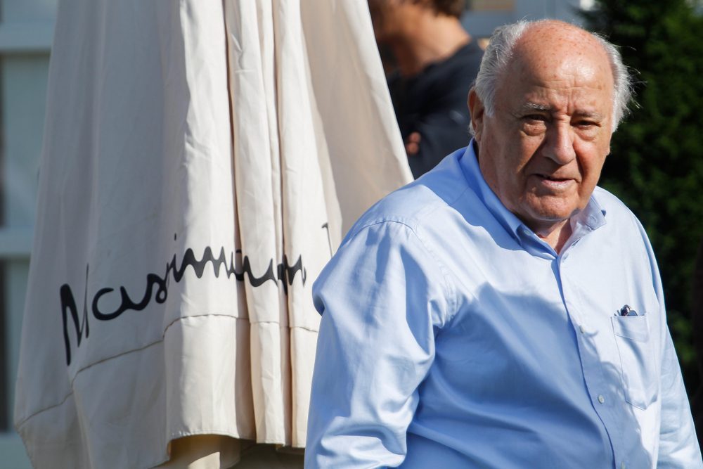 Amancio Ortega, a man in a light blue shirt, stands next to a large, folded umbrella