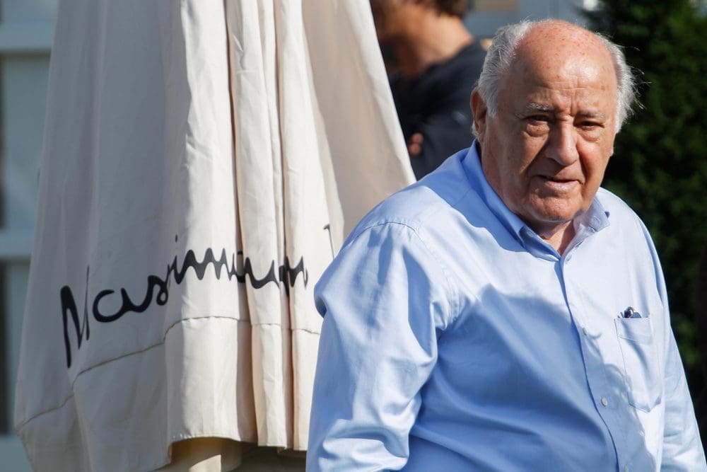 Amancio Ortega, a man in a light blue shirt, stands next to a large, folded umbrella