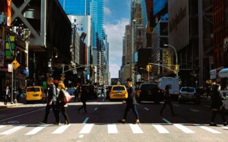 Americans crossing a busy 5th Avenue street in New York City, with taxis and tall buildings