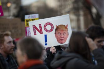 An anti-Trump protester holds a sign with a stylized "NO" and a caricature of the president