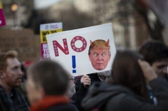 An anti-Trump protester holds a sign with a stylized "NO" and a caricature of the president