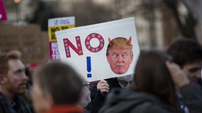 An anti-Trump protester holds a sign with a stylized "NO" and a caricature of the president