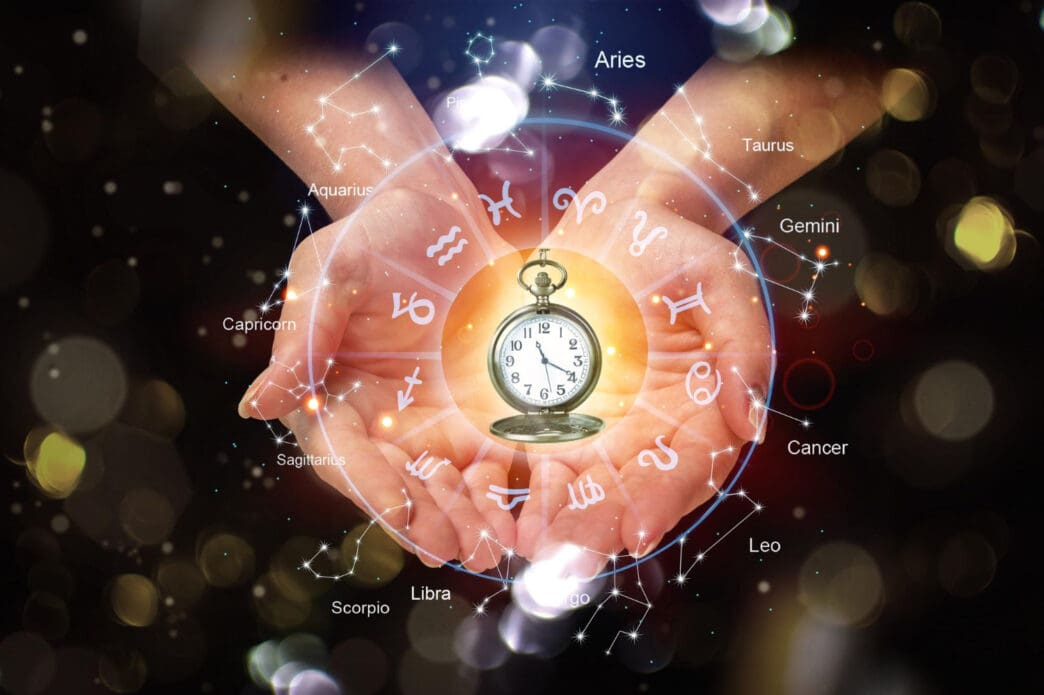 Hands hold a glowing pocket watch, encircled by the twelve symbols and constellations of the zodiac