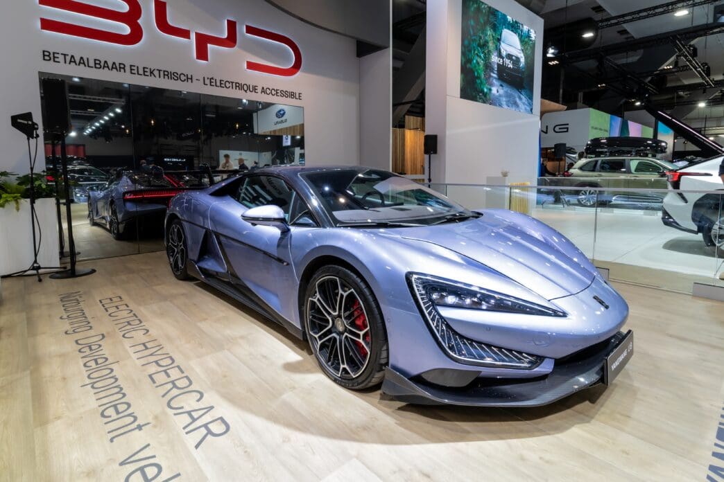 A sleek, blue electric hypercar is displayed at an auto show