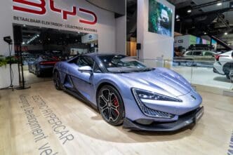 A sleek, blue electric hypercar is displayed at an auto show